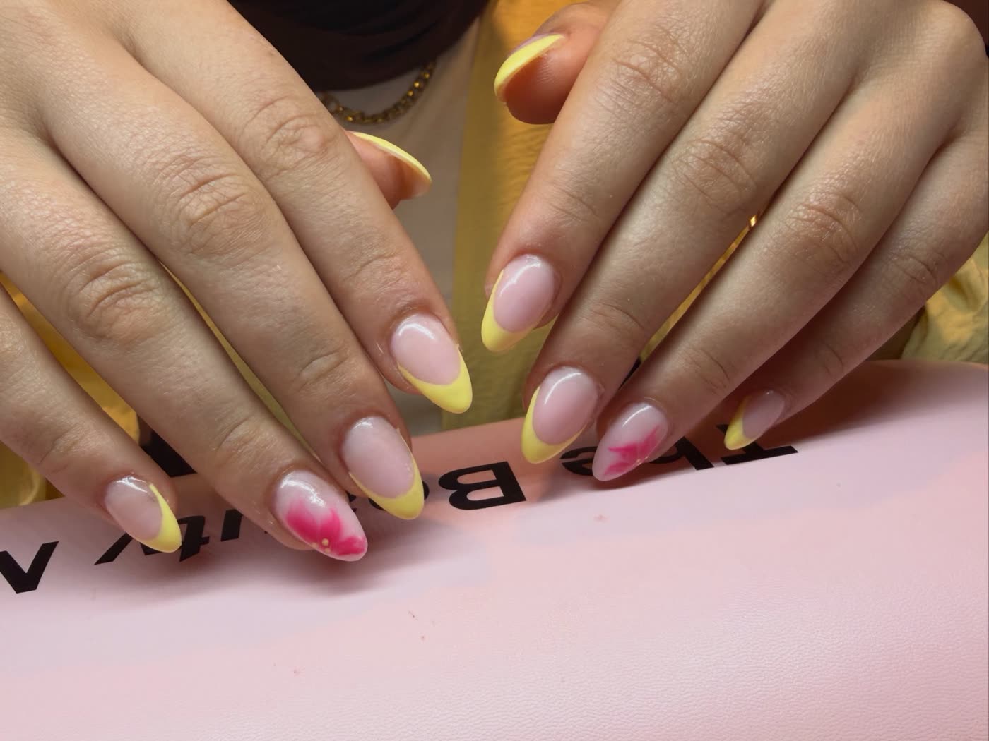 Handen met een french manicure in geel en een bloem op de ringvinger